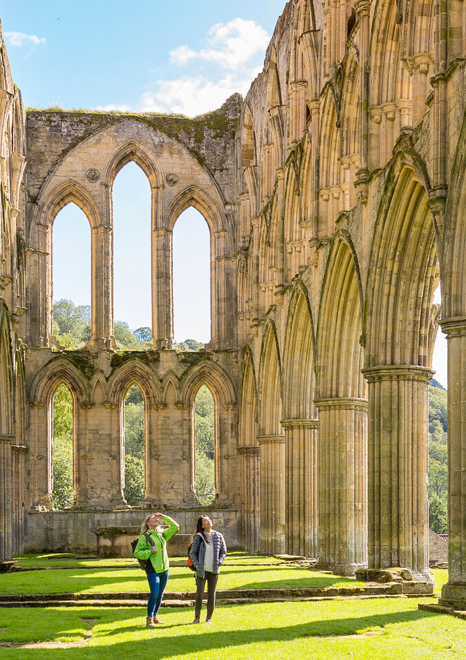 Two people walking among the ruins of an old abbey. Credit VisitBritain / Gary-Walsh.