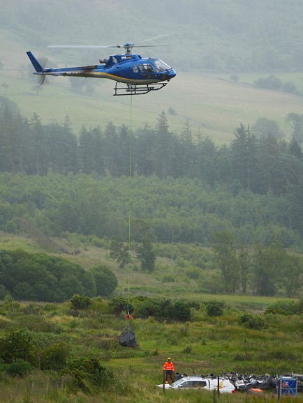 A black bag of heavy stone flies beneath a blue helicopter
