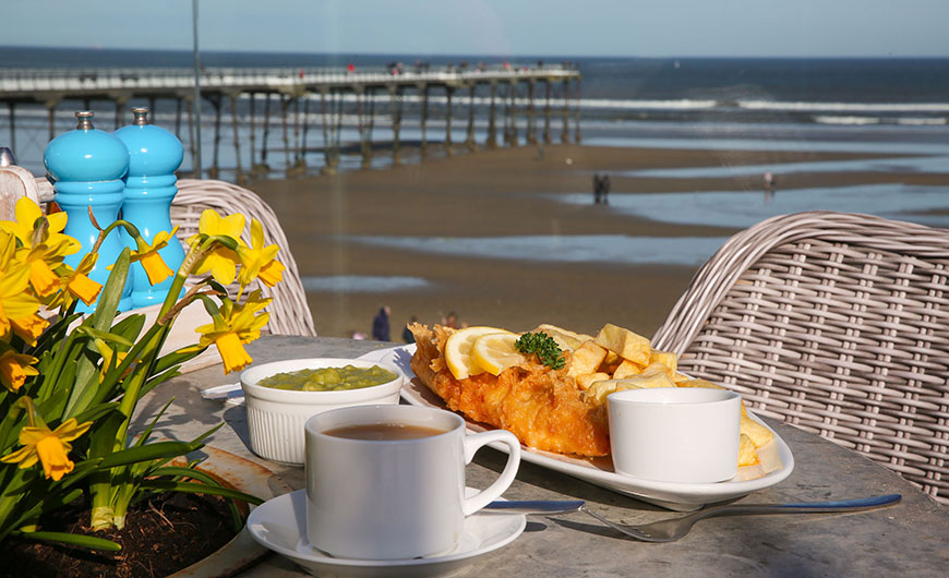 Plated fish and chips with sea view in the background by Ceri Oakes