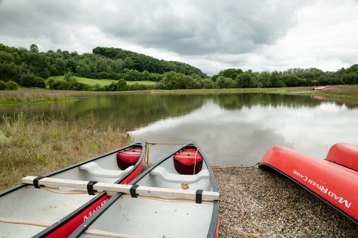 Canoes in the foreground on the edge of a large pond / lake. Credit Charlie Fox.