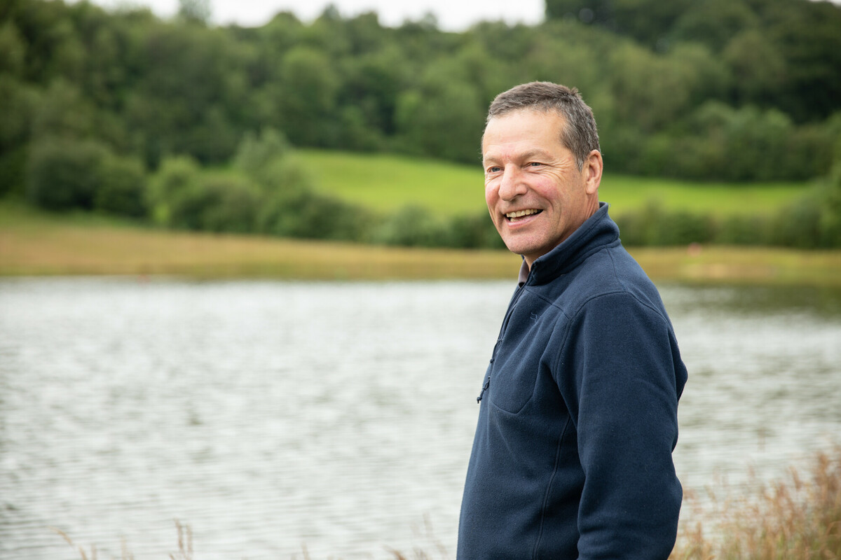 Portrait photo of a person in the foreground with a large pond / lake in the background. Credit Charlie Fox.